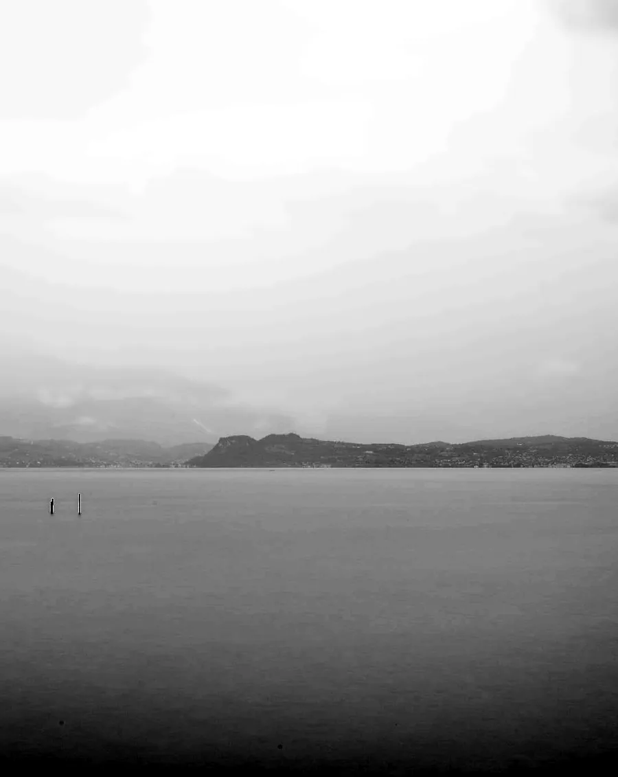 Il lago di Garda coperto dalla nebbia, con due pali che affiorano dall’acqua